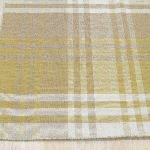 Flatwoven rug with an intersecting yellow, tan, and cream plaid pattern on light wood floor.