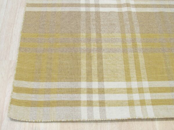 Flatwoven rug with an intersecting yellow, tan, and cream plaid pattern on light wood floor.