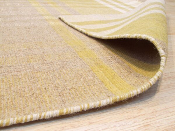 Close-up of a low-pile yellow and beige striped rug folded over on light wood flooring.