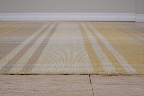 Low-pile yellow, cream, and tan plaid rug rests on light wood plank flooring.