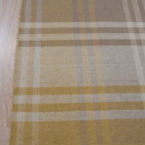Plaid flatweave rug in mustard, tan, and cream colors resting on light wood flooring.
