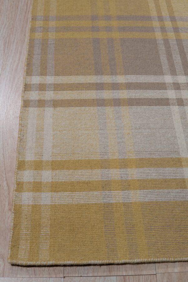 Plaid flatweave rug in mustard, tan, and cream colors resting on light wood flooring.