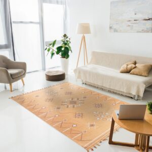 A warm orange flatweave rug with white and brown geometric patterns anchors a bright room with white floors and modern furniture.