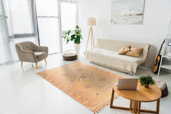 A warm orange flatweave rug with white and brown geometric patterns anchors a bright room with white floors and modern furniture.