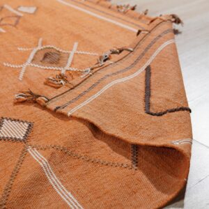 Geometric orange rug with white diamonds and dark accents shown folded slightly on light flooring.