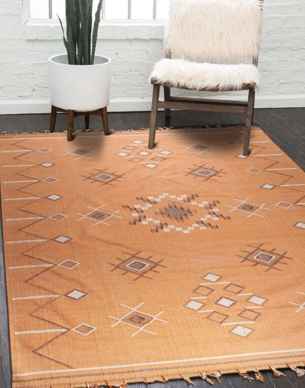 Terracotta flatweave rug featuring diamond motifs lies on dark wood flooring near a white fluffy chair.