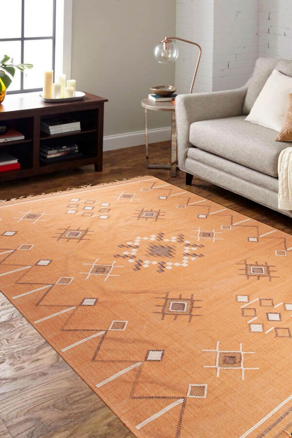Orange flatweave rug with white and brown geometric patterns covers a living room floor beside a gray armchair.