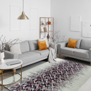 A low-pile rug with fading geometric red and gray patterns sits beneath two light gray sofas.