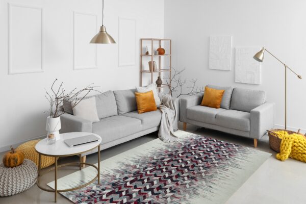 A low-pile rug with fading geometric red and gray patterns sits beneath two light gray sofas.