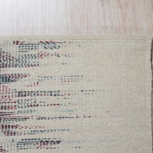 Tightly woven beige rug featuring a speckled dark red and dark blue design on light wood plank flooring.