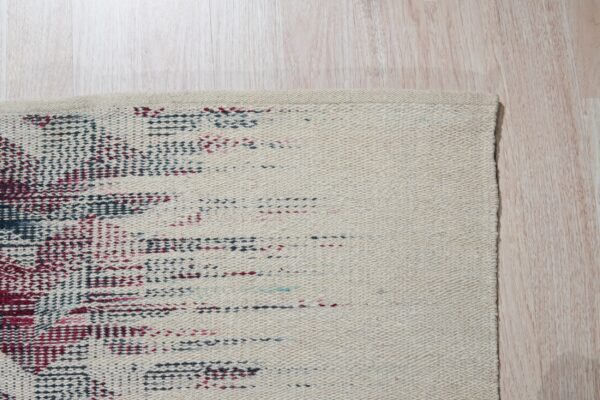 Detail of a cream low-pile rug with abstract red and blue dots on pale wood plank flooring.