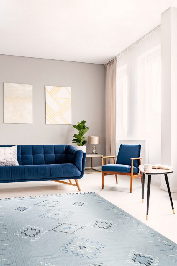 Light blue flatwoven rug with geometric patterns sits beneath a navy velvet sofa and armchair.