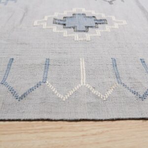 Geometric light blue rug showing white and navy stitched patterns over light wooden flooring.