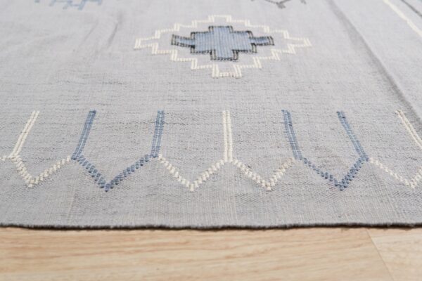 Geometric light blue rug showing white and navy stitched patterns over light wooden flooring.