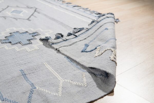 Light gray rug featuring geometric patterns and raised texture, shown folded over on light wood planks.