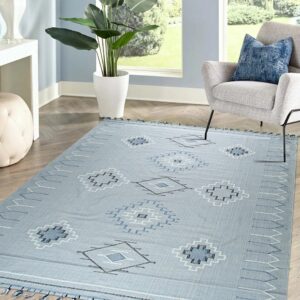 Light blue geometric patterned rug with tassels on herringbone wood floor next to a grey armchair.
