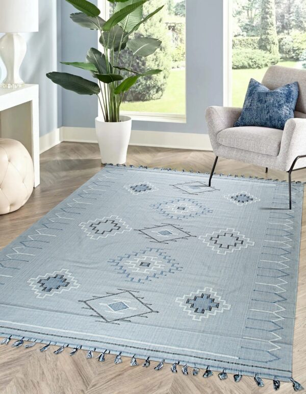 Light blue geometric patterned rug with tassels on herringbone wood floor next to a grey armchair.