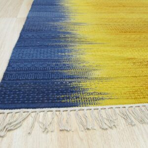 Blue and yellow flatweave rug with textured horizontal stripes and fringe lying on light wood floor.