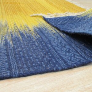 Low-pile rug with yellow to indigo gradient stripes, rolled on a light wood floor.