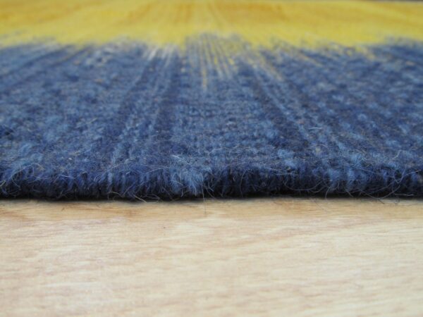 Extreme close-up of a textured blue rug edge with a yellow color gradient on a wooden floor.