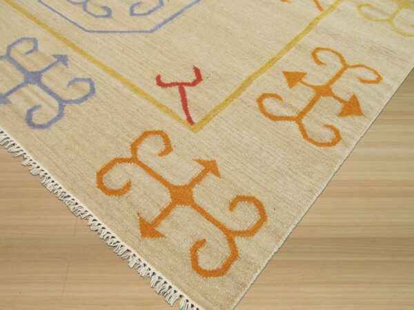 Corner of a low pile cream rug with geometric orange, blue, and red patterns on a wood floor.