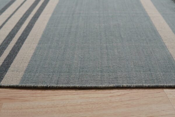 Low-pile dusty blue rug with cream and slate striped border shown on light wooden flooring.
