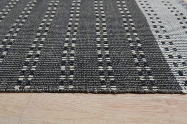 Textured gray rug with dashed vertical stripes and geometric patterns rests on a light wood floor.