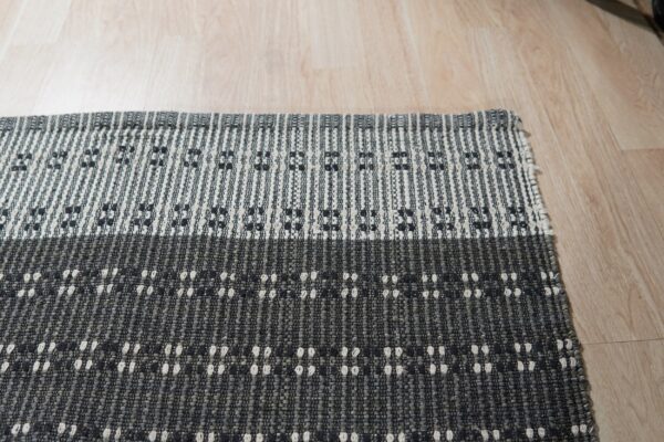 Gray and black striped flatweave rug with small geometric patterns against light wood flooring.