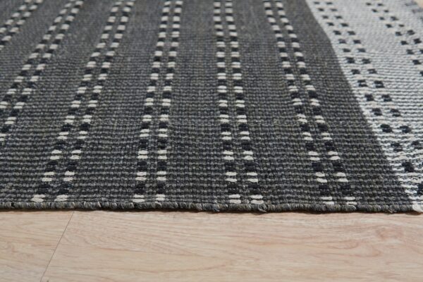 Dark gray textured rug featuring vertical dashed white and black stripe patterns on light wood flooring.