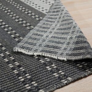 Textured gray and white flat-weave rug with geometric stripes lying on light wood plank flooring.