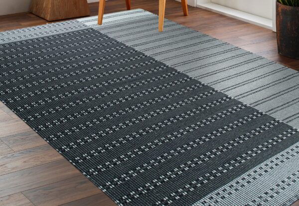 Contrasting gray and black rug with striped and geometric patterns sits on a wood floor.