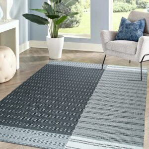A geometric dark gray and light gray flat weave rug sits on herringbone wood flooring in a bright room.