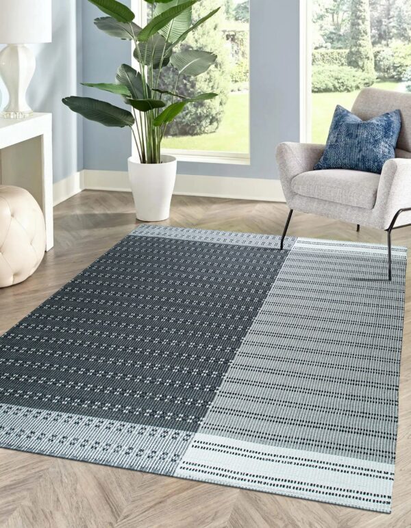 A geometric dark gray and light gray flat weave rug sits on herringbone wood flooring in a bright room.