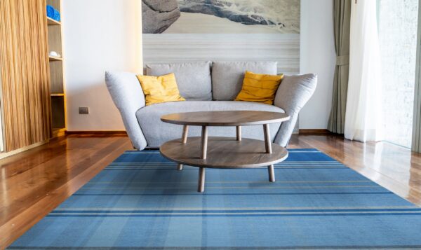 Blue low-pile rug with plaid stripes under a wooden coffee table and a grey sofa on hardwood floors.