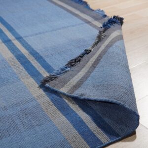 A flatwoven blue and gray striped rug is partially rolled up on a light wood floor.