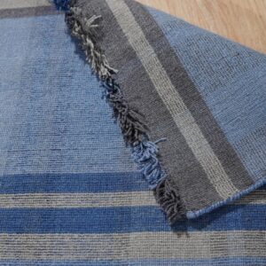 Blue and gray striped flatweave rug is folded over a wooden floor, showing short fringe detail.