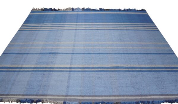 Blue rug with visible low texture and a striped pattern featuring white, gray, and dark blue bands.