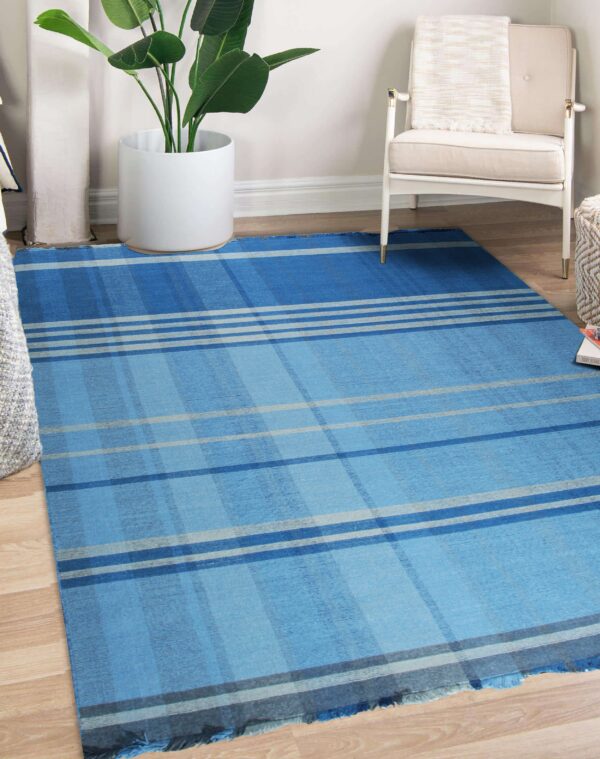 This blue plaid area rug covers wood flooring near a white armchair and potted plant.