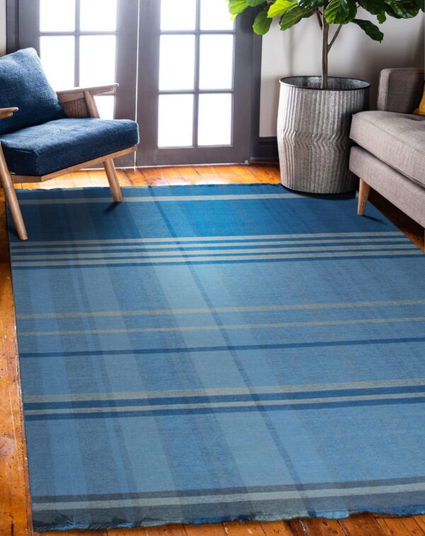 A blue and gray plaid flatweave rug sits on hardwood floors near a wooden chair and gray sofa.