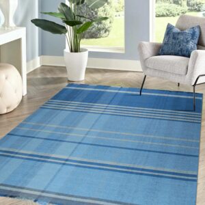 Blue and gray plaid flatweave rug on chevron wood flooring next to a gray armchair and potted plant.