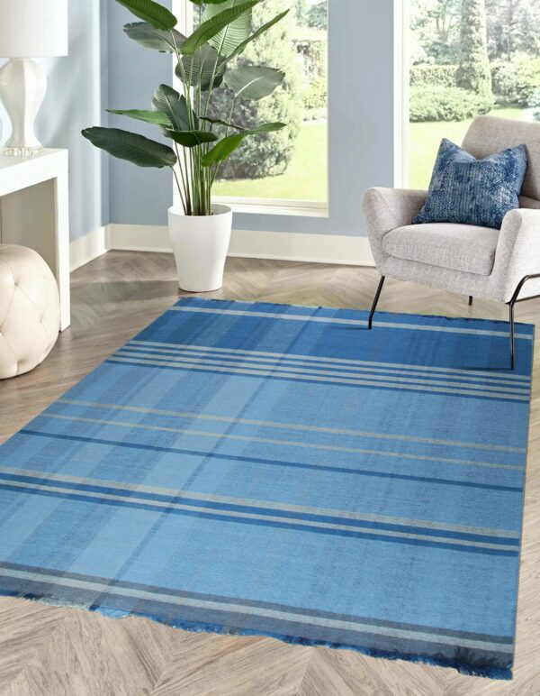 Blue and gray plaid flatweave rug on chevron wood flooring next to a gray armchair and potted plant.