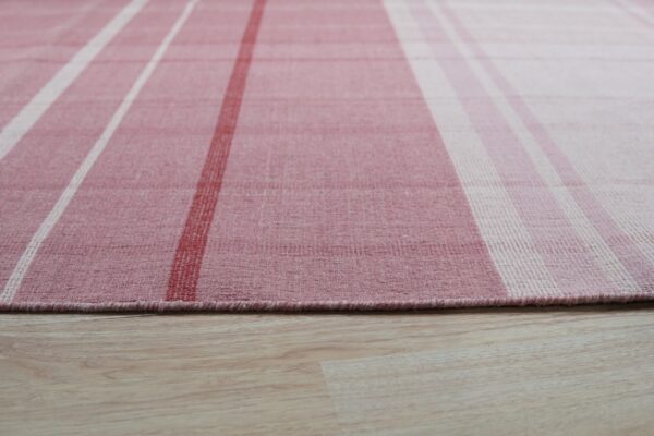 Pink, white, and red plaid low-pile rug resting on light wood-look flooring.