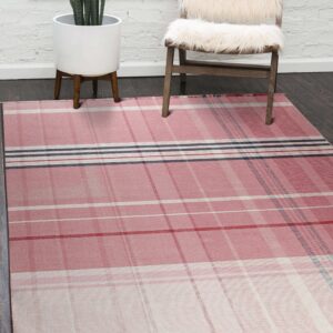 A pink tartan rug rests on dark wood flooring next to a fuzzy white chair and a tall snake plant.