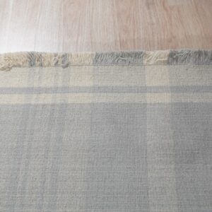 Light gray rug with horizontal cream stripes and mixed tassels lies on pale wood flooring.