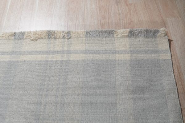Light gray rug with horizontal cream stripes and mixed tassels lies on pale wood flooring.