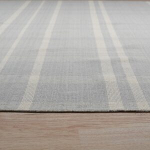 A gray and cream striped low-pile rug with fringe rests on light blonde wood flooring.