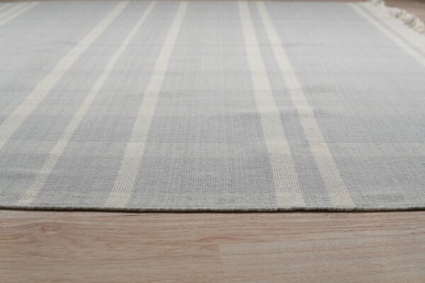 A gray and cream striped low-pile rug with fringe rests on light blonde wood flooring.