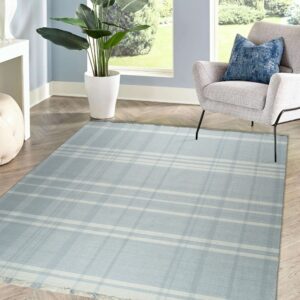 A low-pile blue and white plaid rug sits on herringbone wood flooring next to a gray chair and large window.