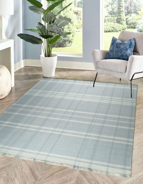 A low-pile blue and white plaid rug sits on herringbone wood flooring next to a gray chair and large window.