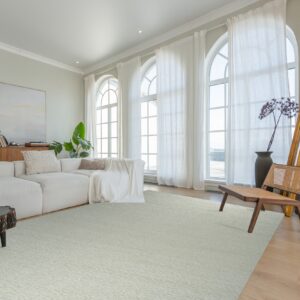 Light green textured rug grounds a living room with a white sectional, wood chair, and large arched windows.